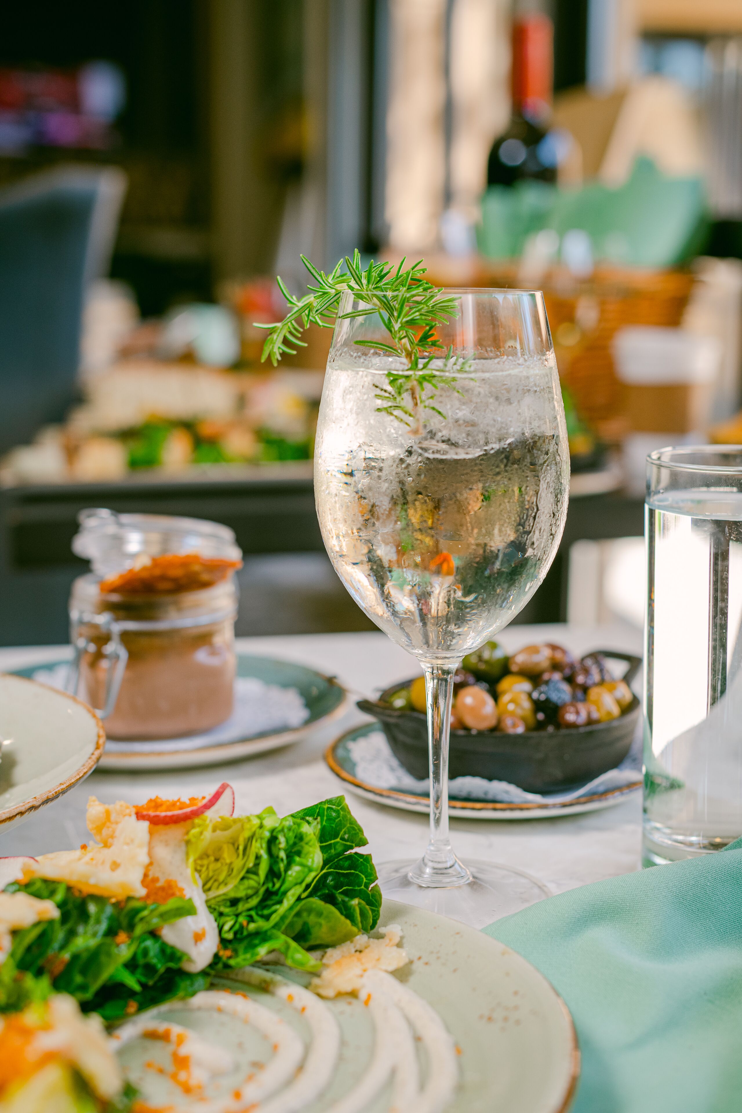 Una mesa de comedor con un vaso de agua, un vaso de vino y un cuenco de aceitunas.