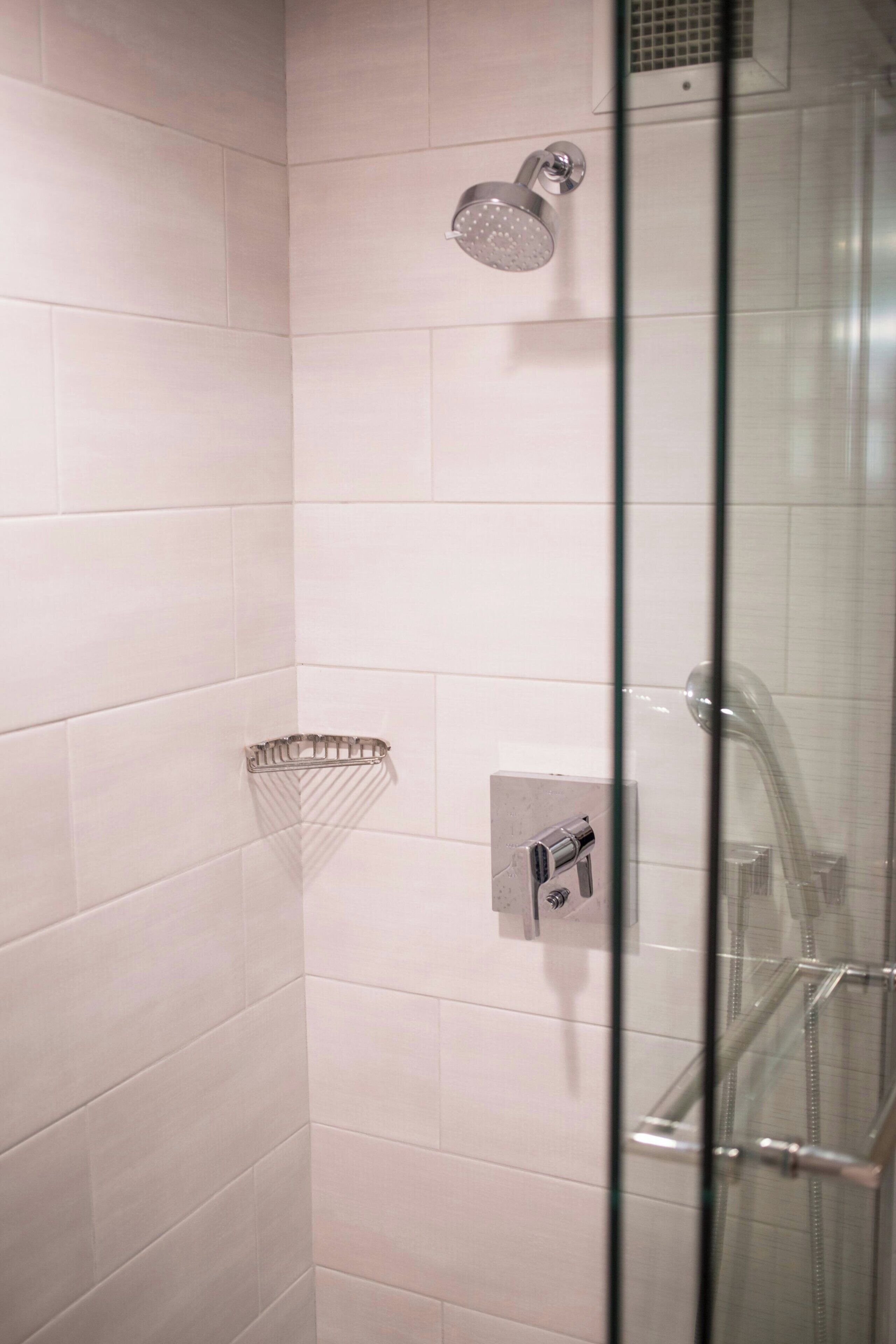 A glass-enclosed shower with a handheld showerhead and a wall-mounted control panel.
