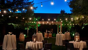 An outdoor dining area with round tables covered in white tablecloths, wooden chairs, and string lights. - Napa Valley Marriott Hotel & Spa (Napa)