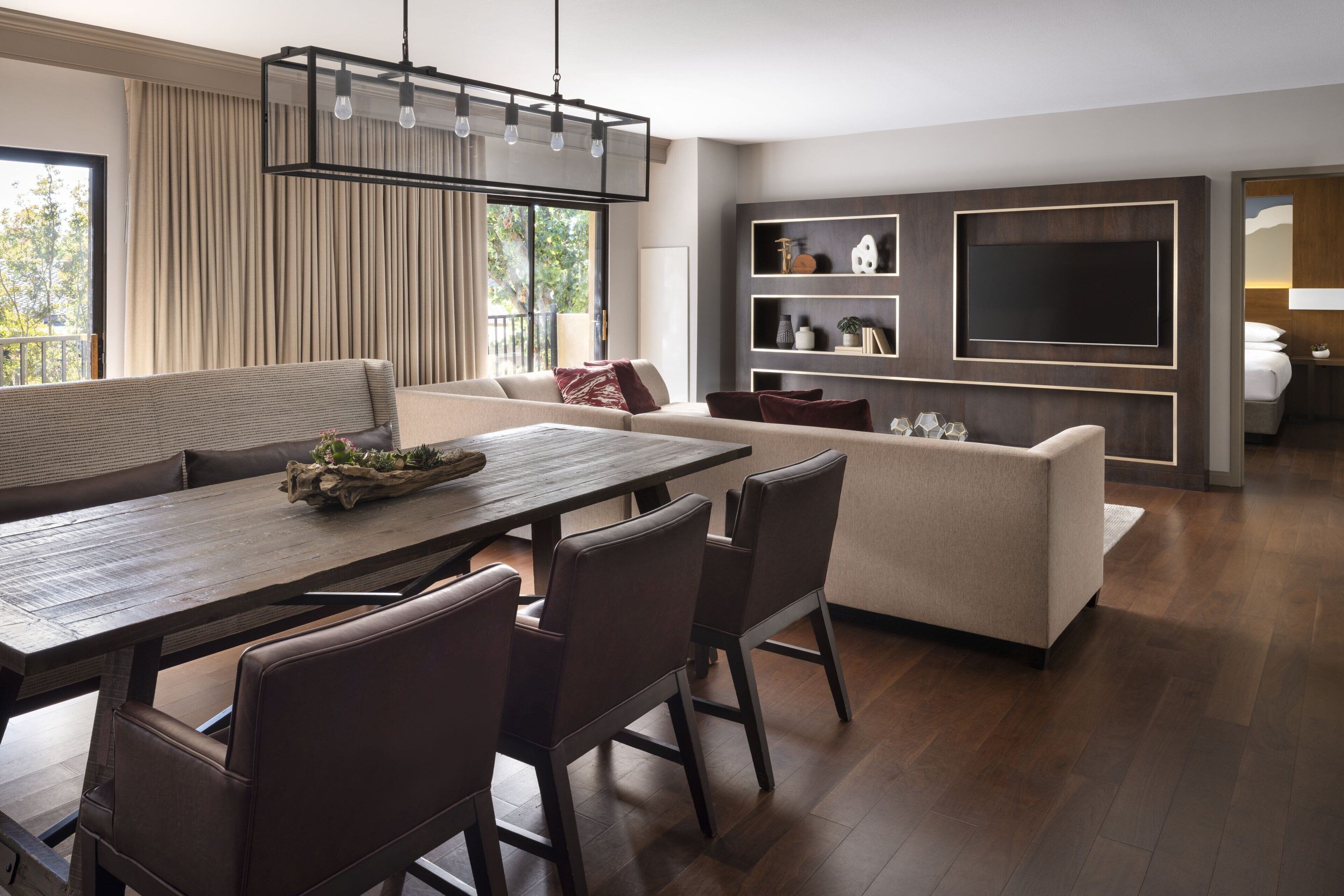 Uma sala de estar moderna com área de jantar, sofá, TV fixada na parede e uma janela grande com cortinas.