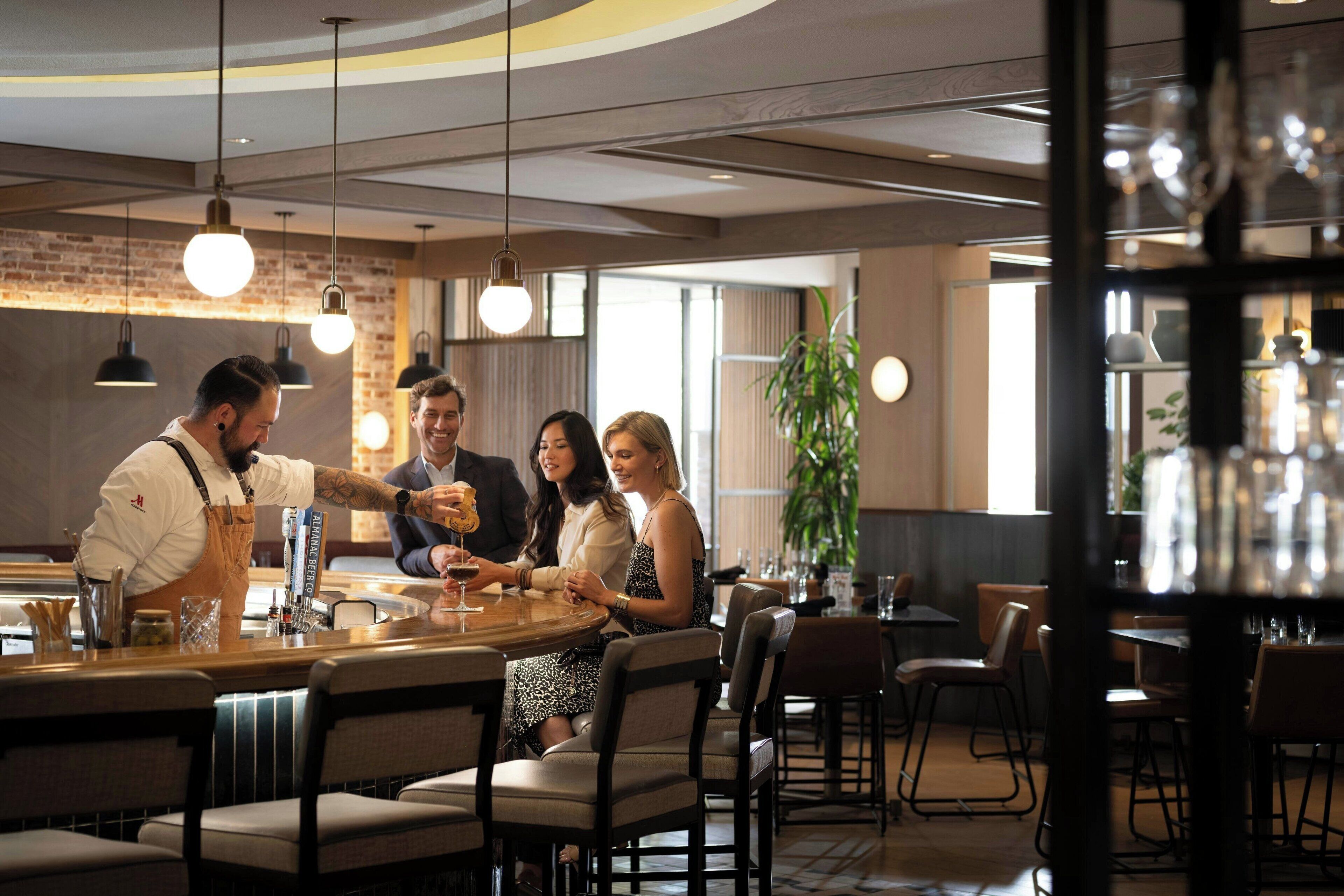 A restaurant interior with a bar area, multiple tables, and hanging pendant lights.