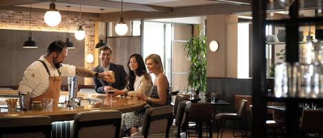 A restaurant interior with a bar area, multiple tables, and hanging pendant lights.
