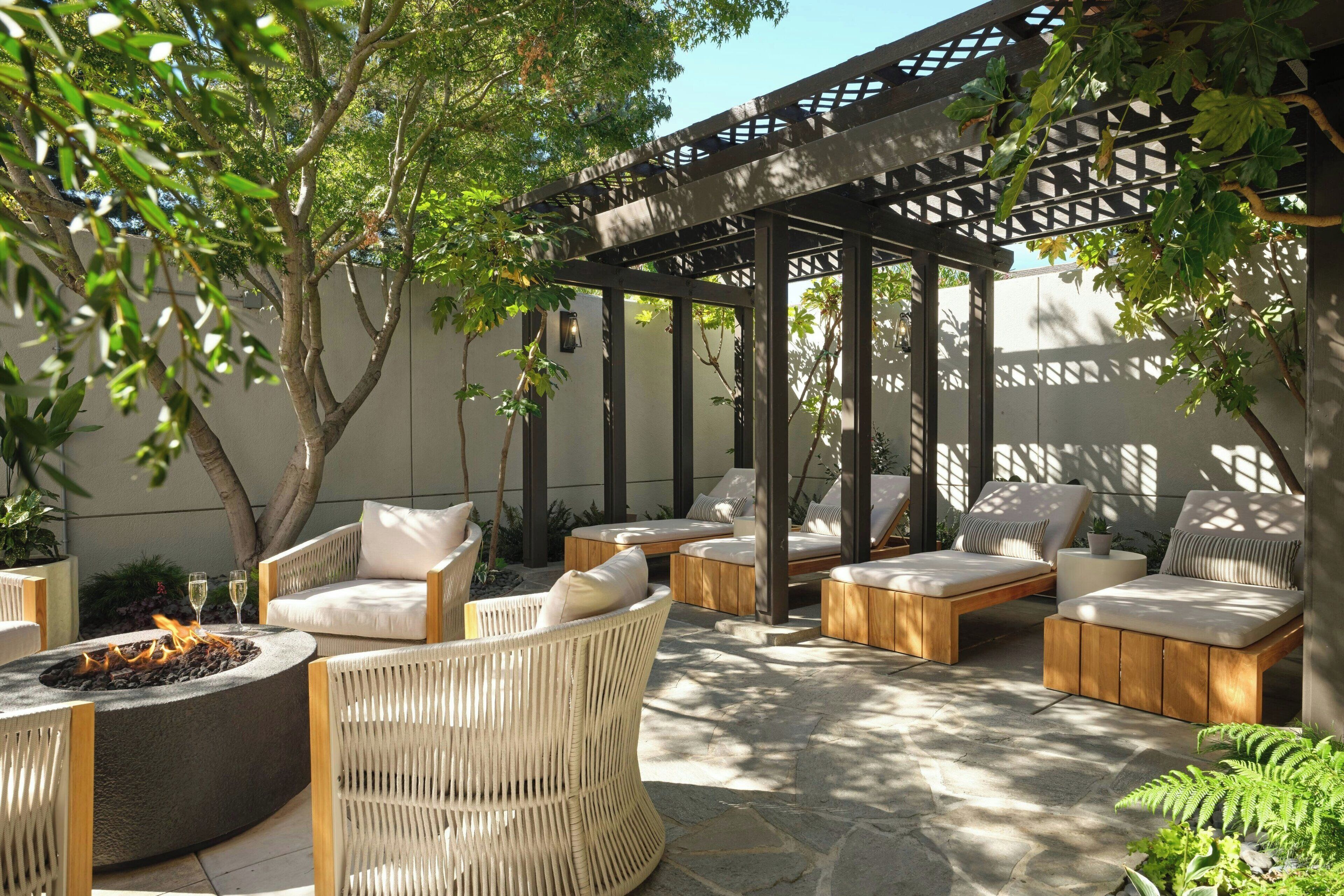 Een terras met rieten meubilair, een vuurplaats en een pergola.