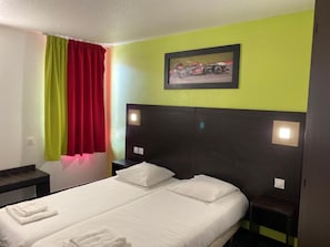 A hotel room with a bed, two bedside tables, a headboard, a window with curtains, and a framed picture on the wall.