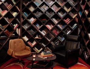 A room with a large bookshelf filled with books, two leather chairs, and a small round table with a candle. - Brown Acropol, a Member of Brown Hotels (Athens)