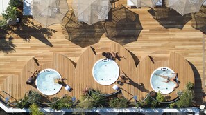 An aerial view of a rooftop with three hot tubs surrounded by wooden decking and outdoor furniture. - Brown Acropol, a Member of Brown Hotels (Athens)