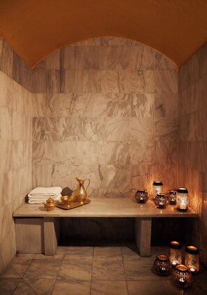 A bathroom with marble walls, a bench, and a sink area with a golden pitcher and bowls. - Brown Acropol, a Member of Brown Hotels (Athens)