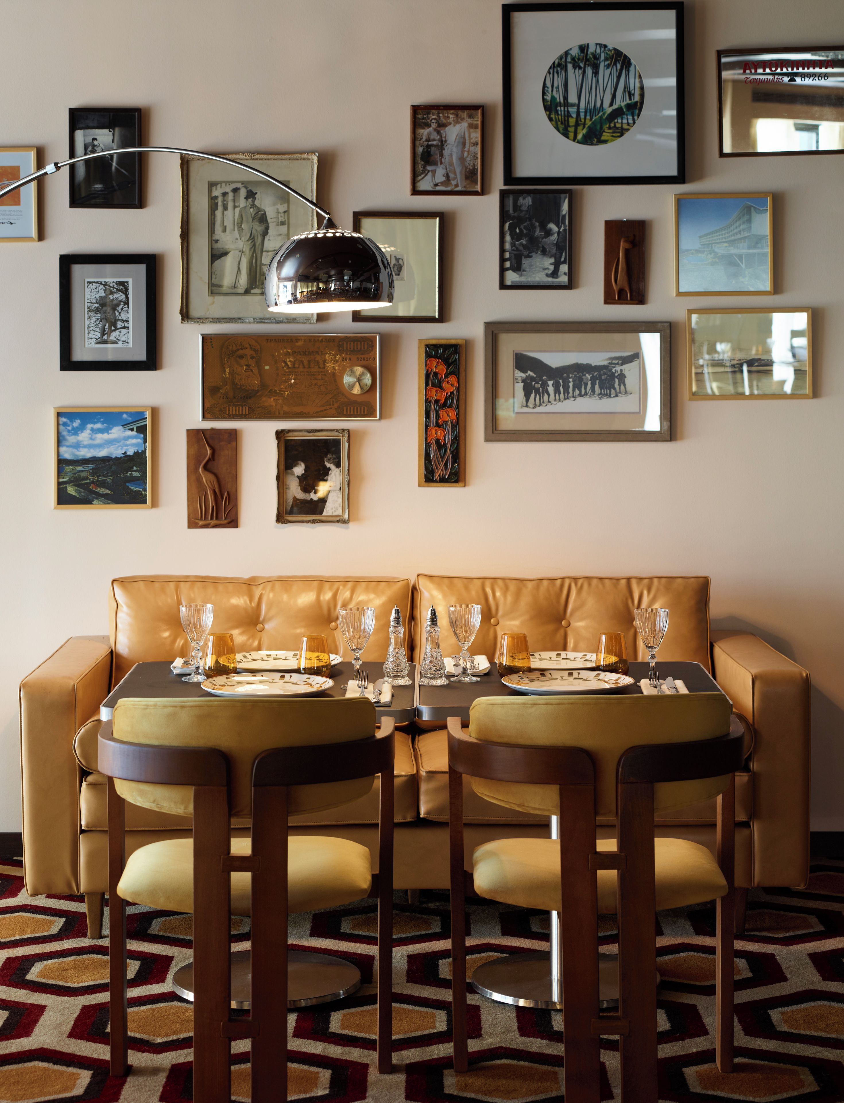 A dining area with a brown leather sofa and two matching chairs, a table set with dinnerware and glasses, and a wall adorned with various framed pictures.