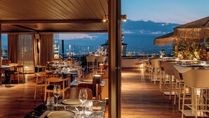 A restaurant with tables set for dining, a view of the cityscape, and a mountain in the background. - Brown Acropol, a Member of Brown Hotels (Athens)