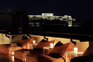 A rooftop terrace with modern seating and a view of a historic building at night. - Brown Acropol, a Member of Brown Hotels (Athens)