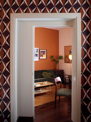 A room with a patterned wall, a sofa, a chair, a table with a lamp, and framed pictures on the wall. - Brown Acropol, a Member of Brown Hotels (Athens)