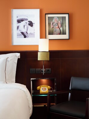 Una camera d'albergo con un letto, una sedia, un telefono e due quadri appesi al muro.
