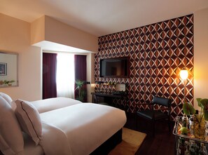 A hotel room with a large bed, a desk with a computer, a TV, and a patterned wall. - Brown Acropol, a Member of Brown Hotels (Athens)