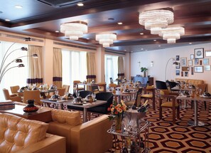 A hotel dining area with multiple tables, chairs, and a bar area with a large ice bucket. - Brown Acropol, a Member of Brown Hotels (Athens)