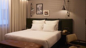 A hotel room with a large bed, a bedside table with a telephone, a chair, and a patterned wall. - Brown Acropol, a Member of Brown Hotels (Athens)