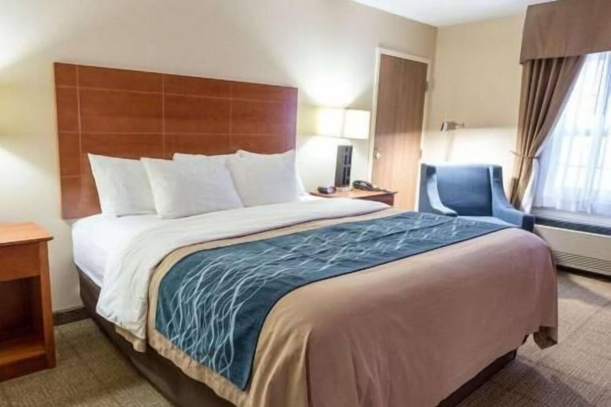 A hotel room with a bed, bedside table, chair, and window with curtains.