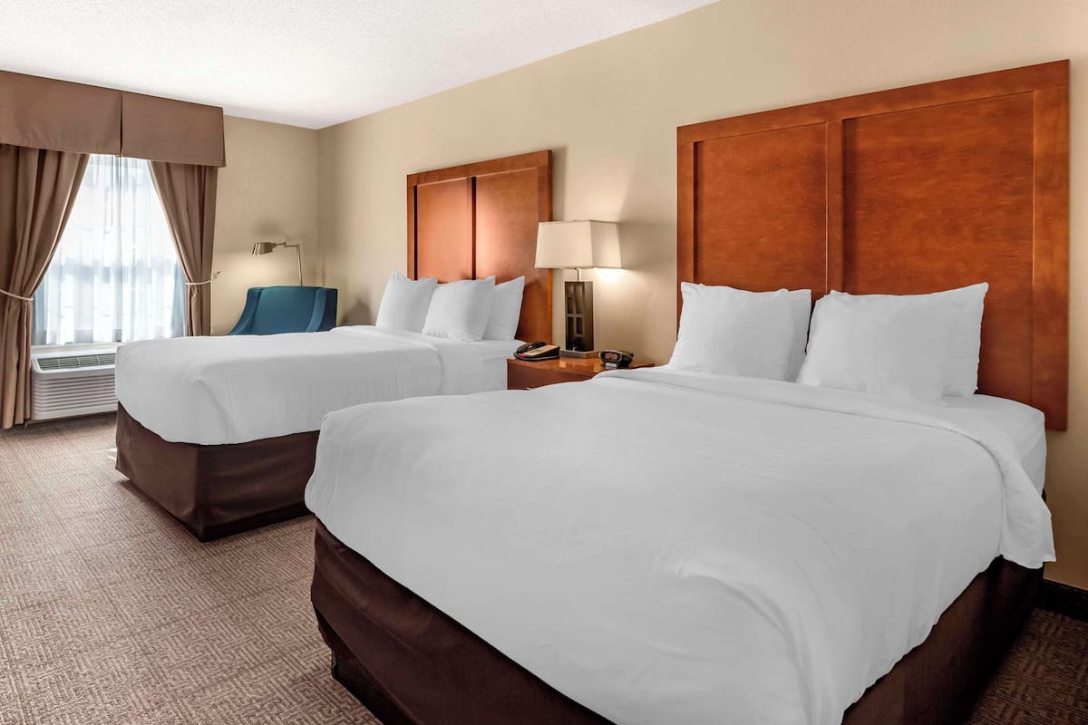 A hotel room with two beds, a desk, a chair, and a window with curtains.