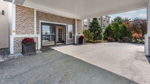 A covered parking area with a brick building entrance, potted plants, and a clear view of the surrounding trees and buildings. - Comfort Inn Augusta (Augusta)
