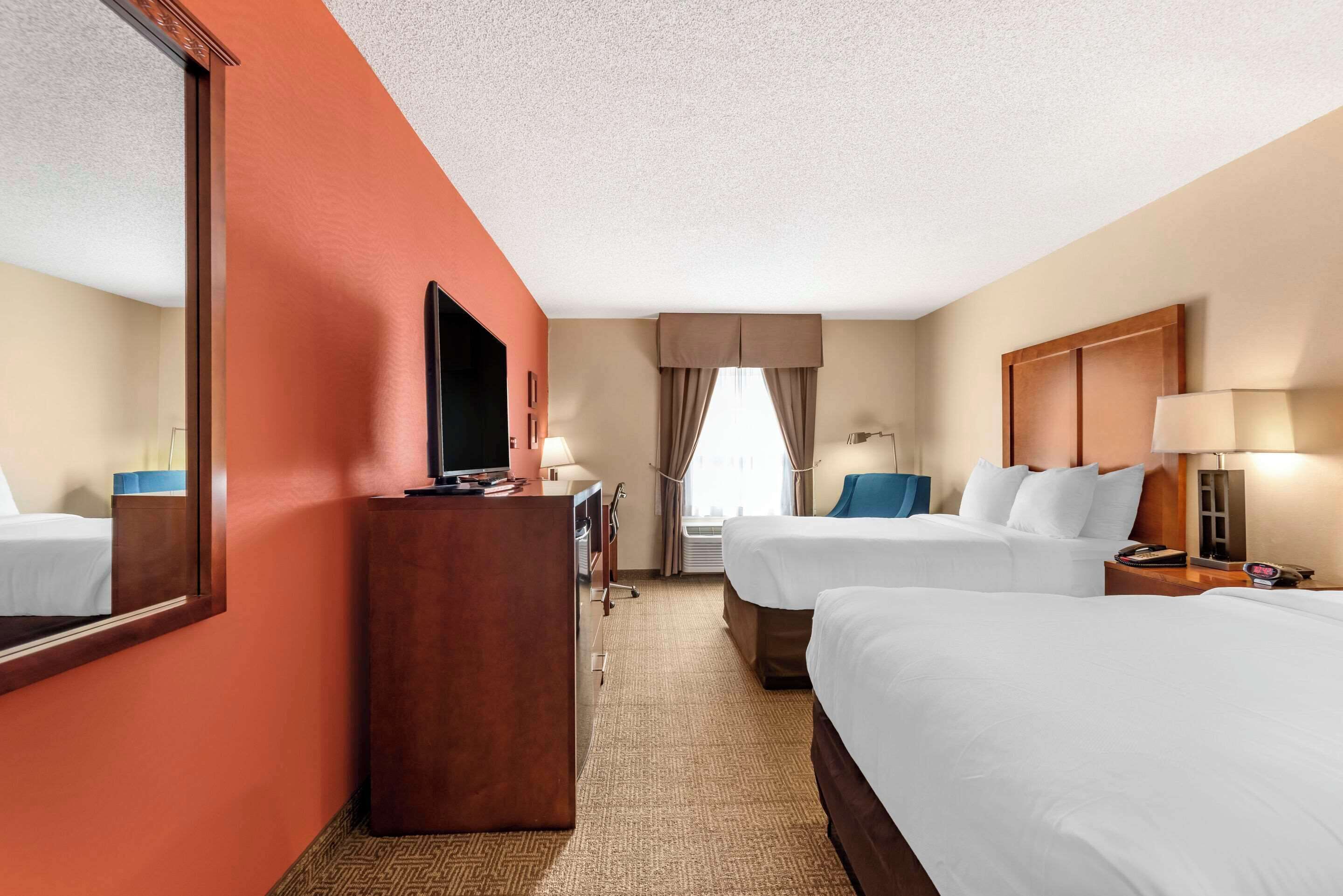 A hotel room with two beds, a desk, a TV, and a large mirror.