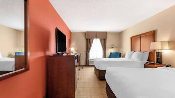 A hotel room with two beds, a desk, a TV, and a large mirror.