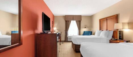 A hotel room with two beds, a desk, a TV, and a large mirror.