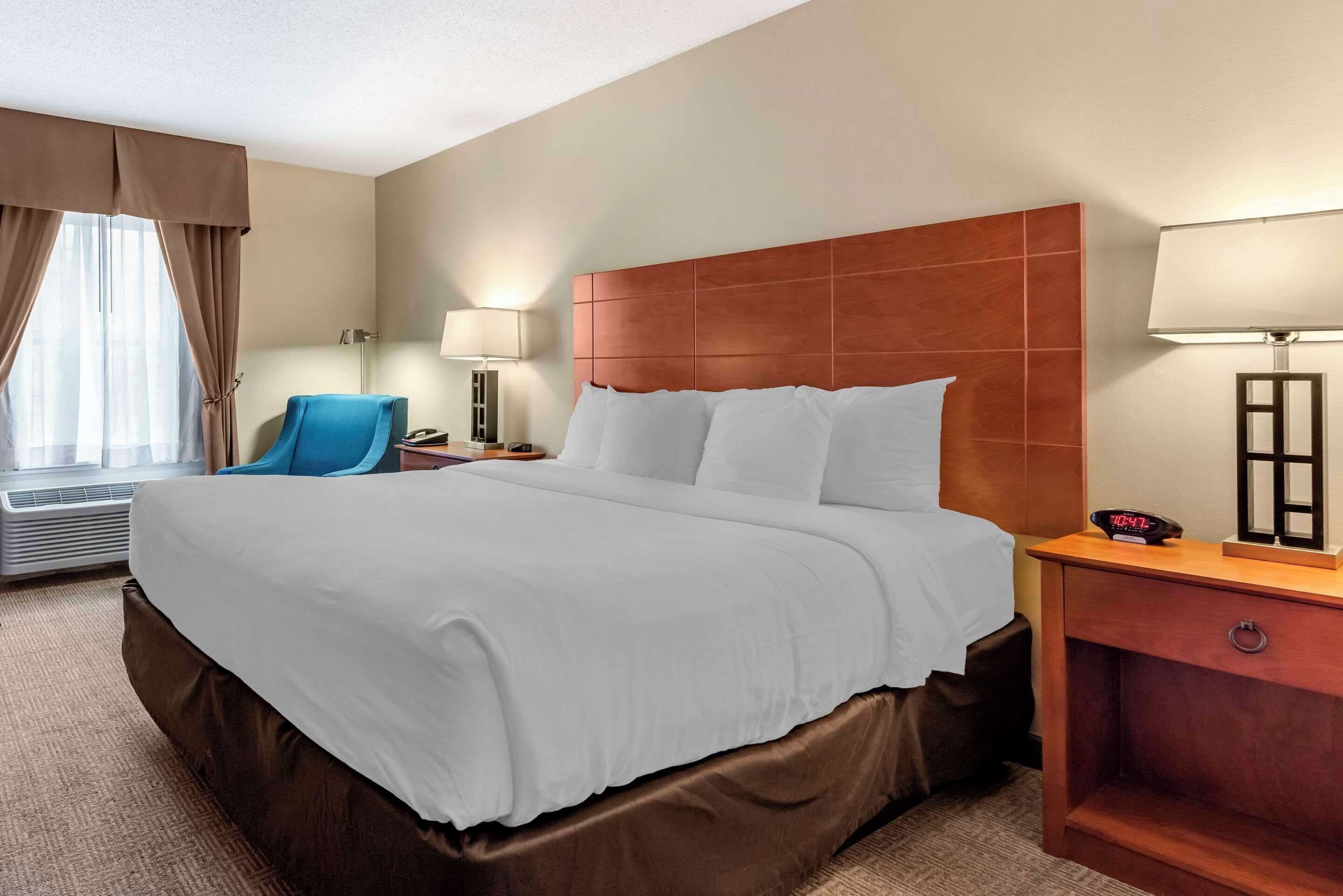 Habitación de hotel con una cama grande, un escritorio con lámpara, una silla y una ventana con cortinas.