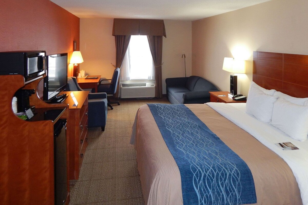 A hotel room with a bed, desk, chair, TV, and a window with curtains.