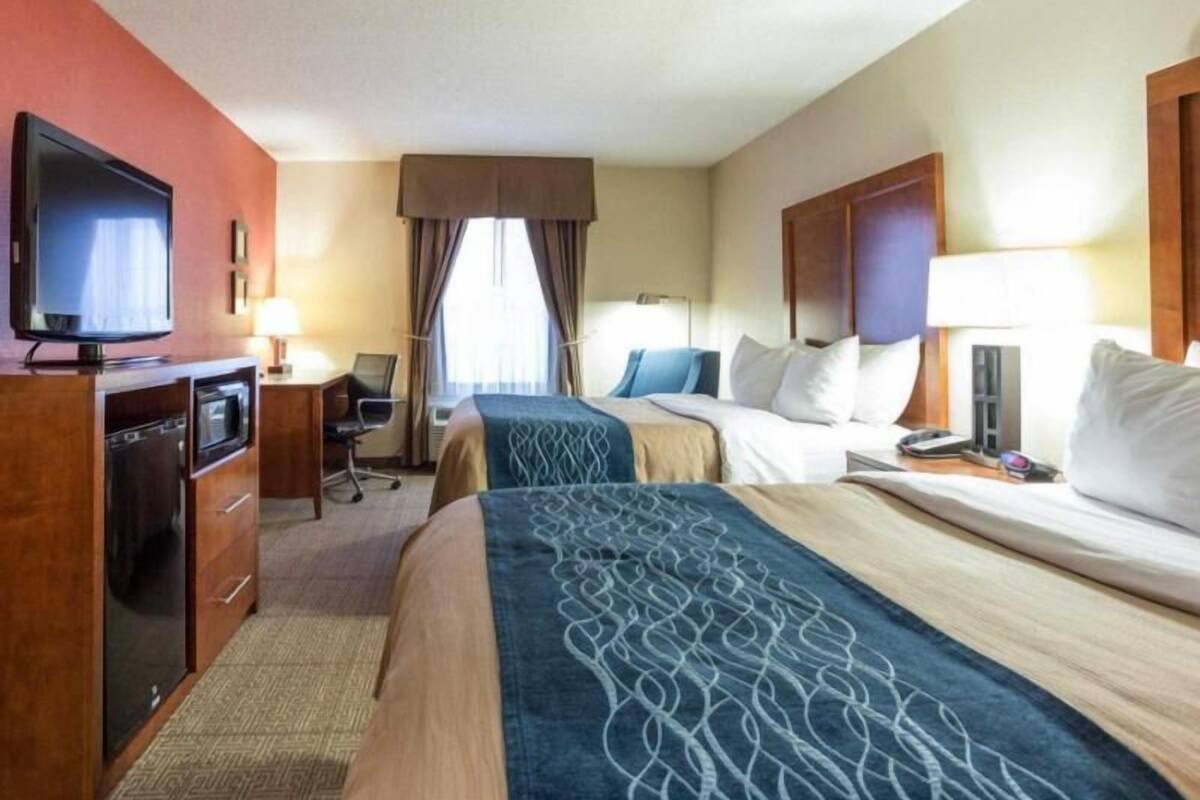 A hotel room with a television, desk, two beds, and a window with curtains.