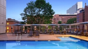 A swimming pool with lounge chairs and umbrellas, surrounded by buildings and trees. - Wyndham Boston Beacon Hill (Boston)