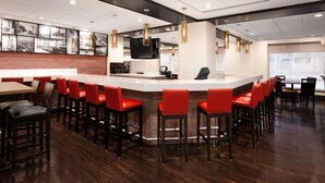 A modern bar area with a central counter, red bar stools, and a brick accent wall. - Wyndham Boston Beacon Hill (Boston)