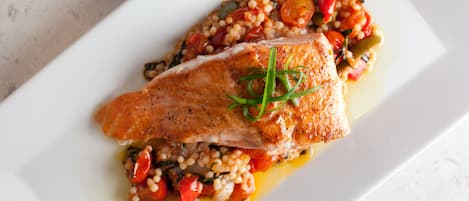 A white rectangular plate with a piece of cooked fish, cherry tomatoes, and a garnish of green herbs.
