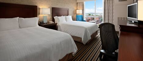 Une chambre d’hôtel avec deux lits, une télévision, un bureau et une vue sur la ville.