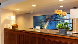 A hotel reception area with a wooden reception desk, a fruit bowl, a potted plant, a large abstract painting, and a sign for member check-in. - Wyndham Boston Beacon Hill (Boston)