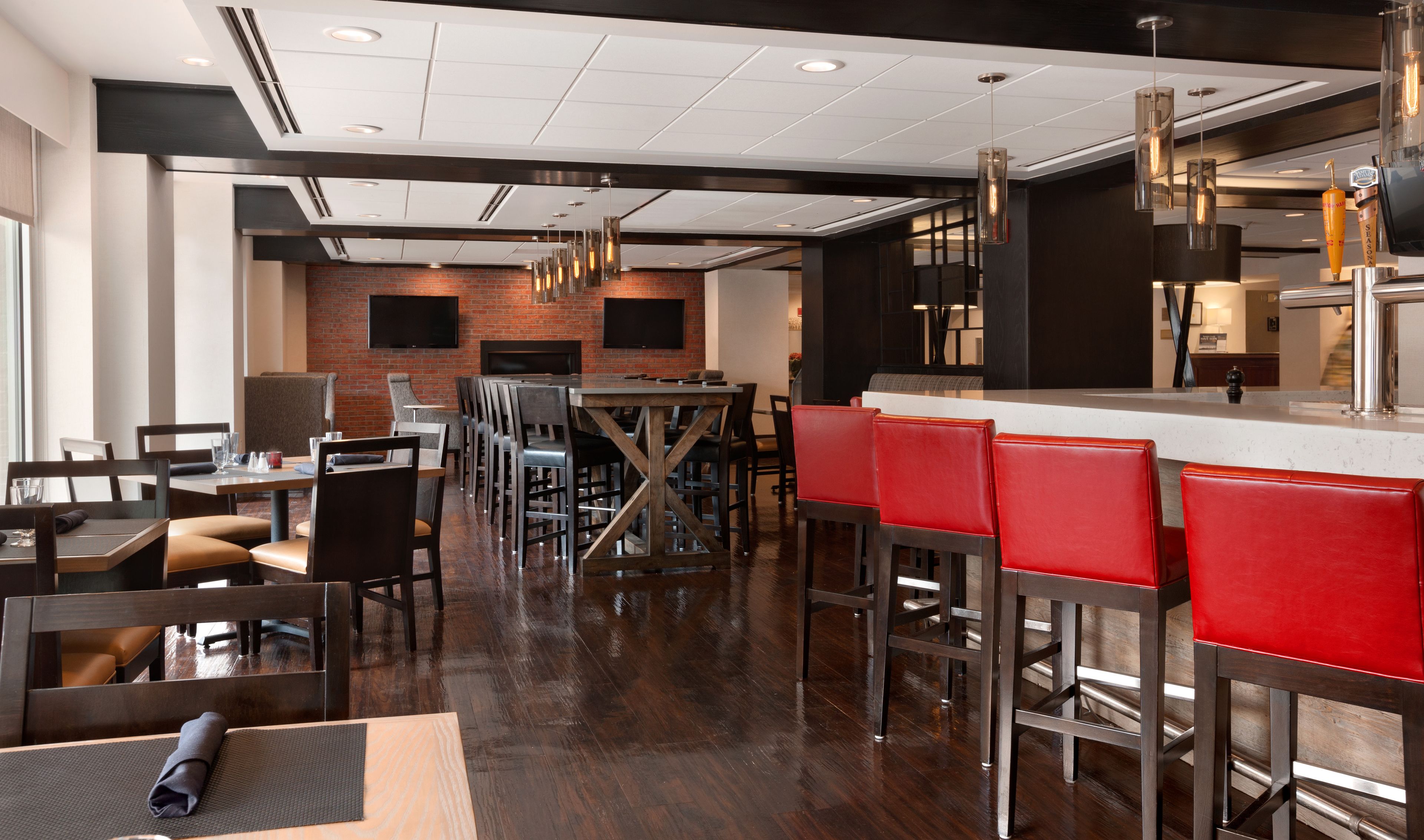 Un restaurante moderno con pared de ladrillo, mesas de madera y taburetes de bar rojos.