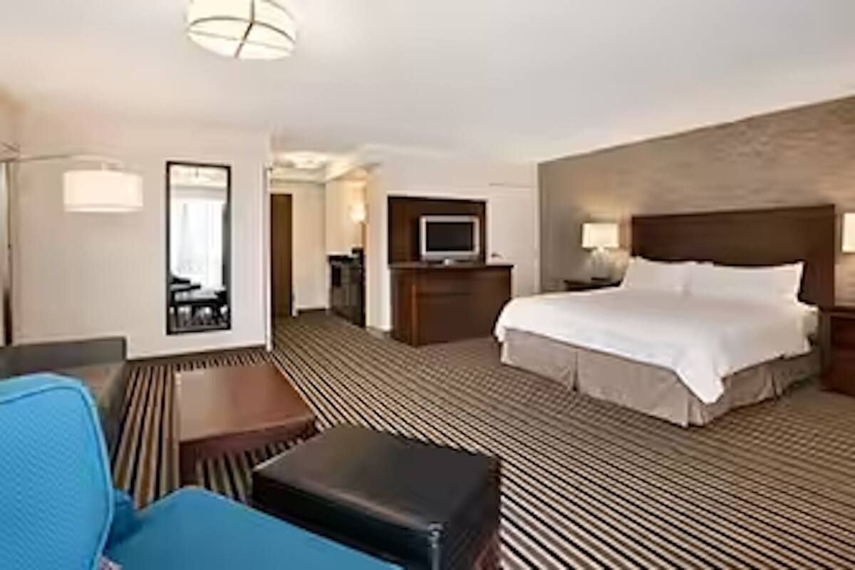 A hotel room with a large bed, a desk, a chair, a television, and a mirror.