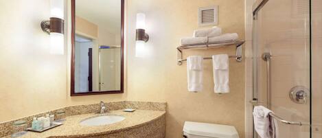 Une salle de bain équipée d’un lavabo en granit, de toilettes, d’une douche à parois de verre et de deux porte-serviettes fixés au mur.