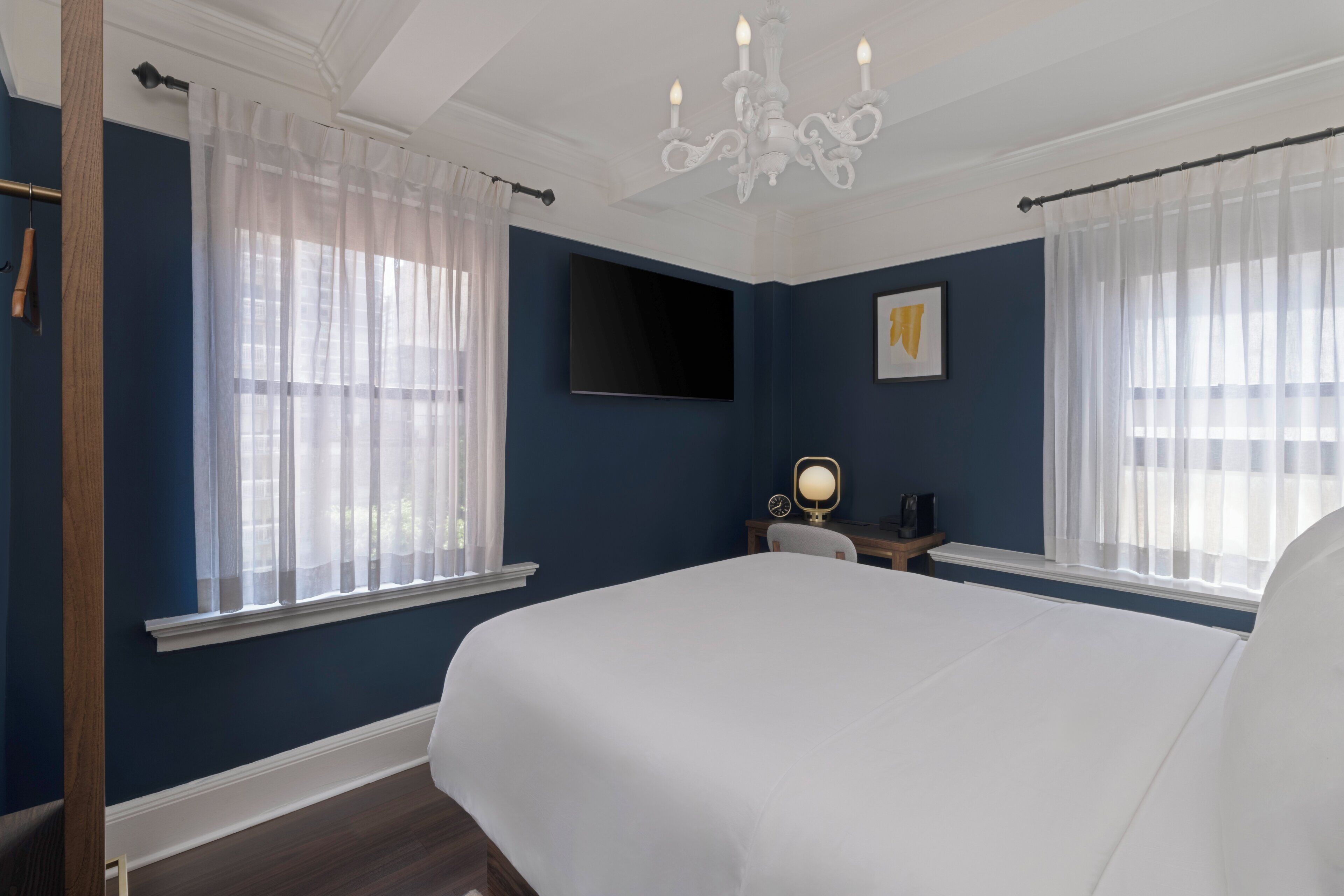 A bedroom with a large bed, a TV mounted on the wall, and a desk with a lamp.