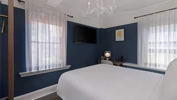 A bedroom with a large bed, a TV mounted on the wall, and a desk with a lamp.