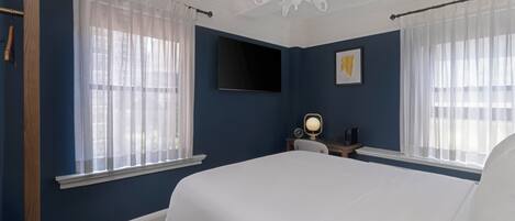A bedroom with a large bed, a TV mounted on the wall, and a desk with a lamp.