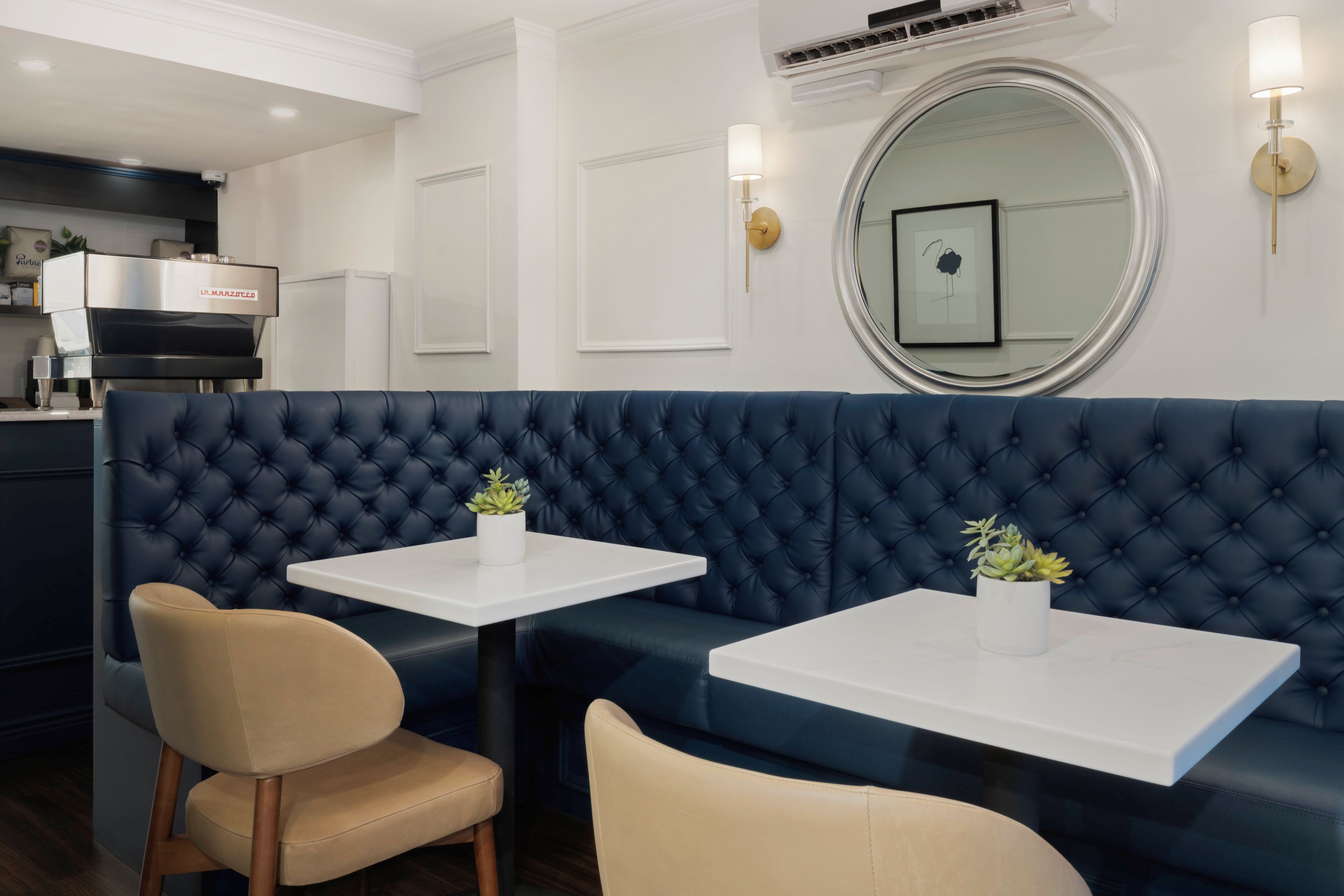 A modern dining area with a dark blue upholstered booth, white tables, and beige chairs.
