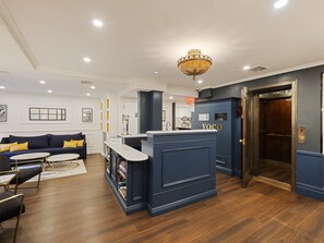 A modern hotel lobby with a dark blue reception desk, a sofa with yellow cushions, and a chandelier. - voco The Franklin New York by IHG (New York)