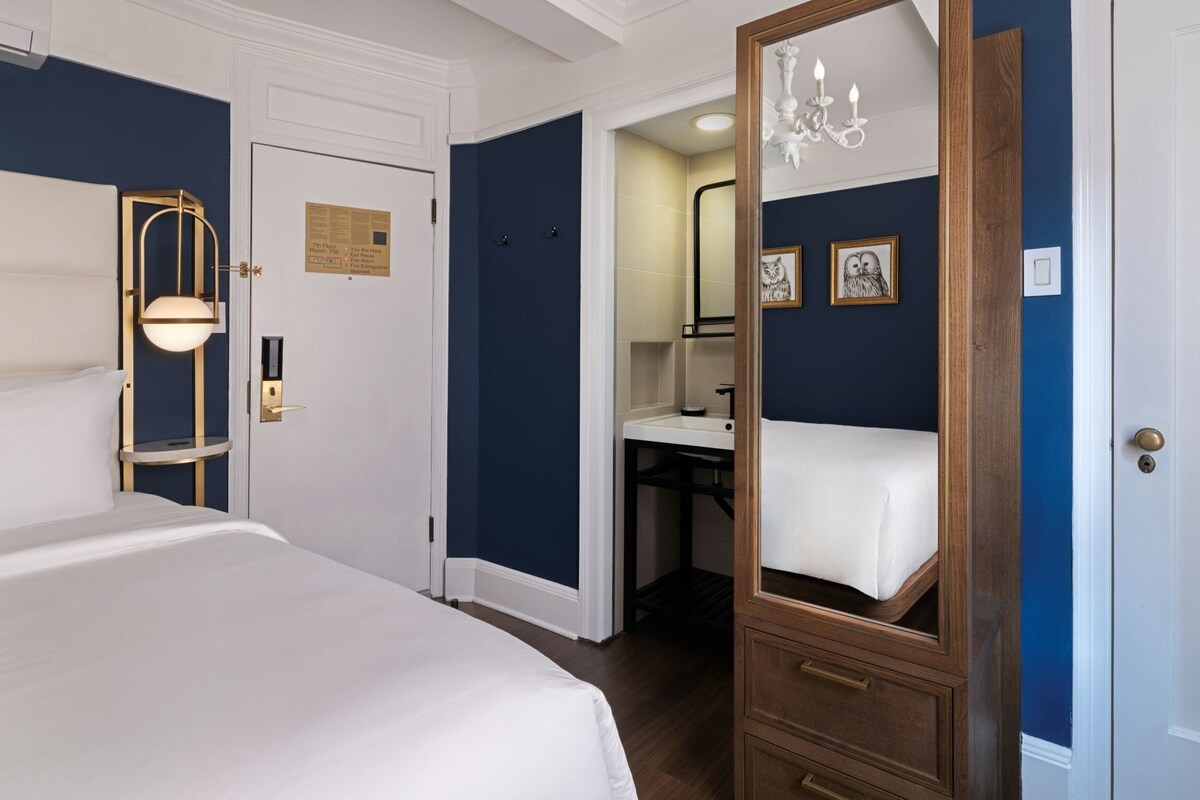 A hotel room with a bed, a mirror, a vanity, and a chandelier.