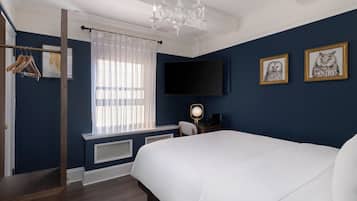 Un dormitorio con una cama grande, un televisor montado en la pared, un escritorio con una silla y una ventana con cortinas ligeras.