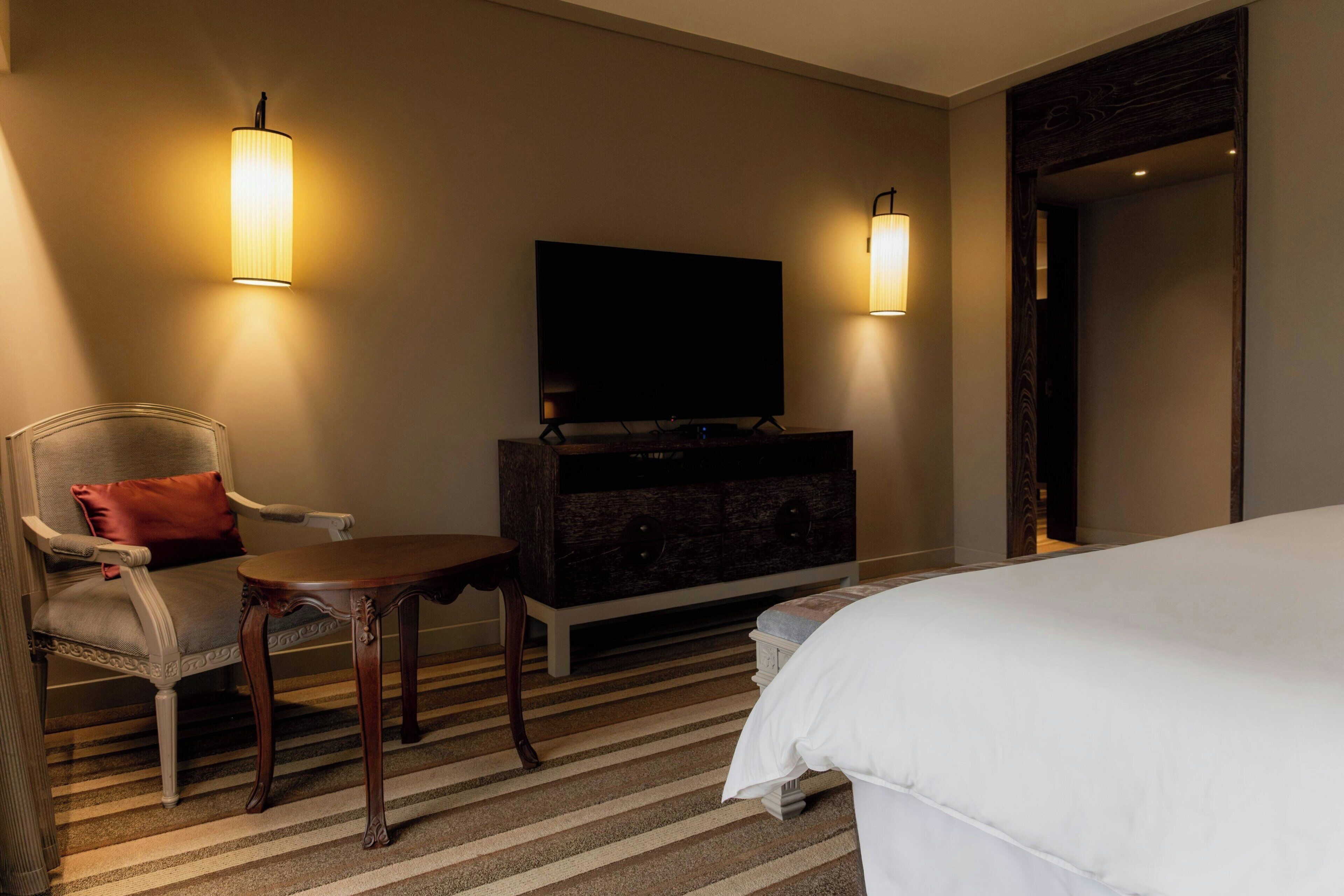 A hotel room with a bed, a TV, a chair, a table, and a dresser.