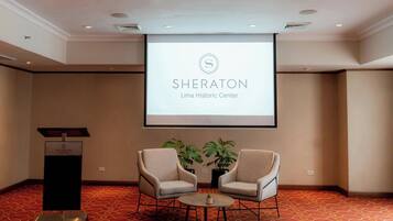 Una sala de conferencias con el logotipo de Sheraton, dos sillas, un atril y una pantalla de proyector.