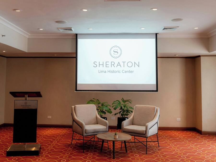 Una sala de conferencias con el logotipo de Sheraton, dos sillas, un atril y una pantalla de proyector.