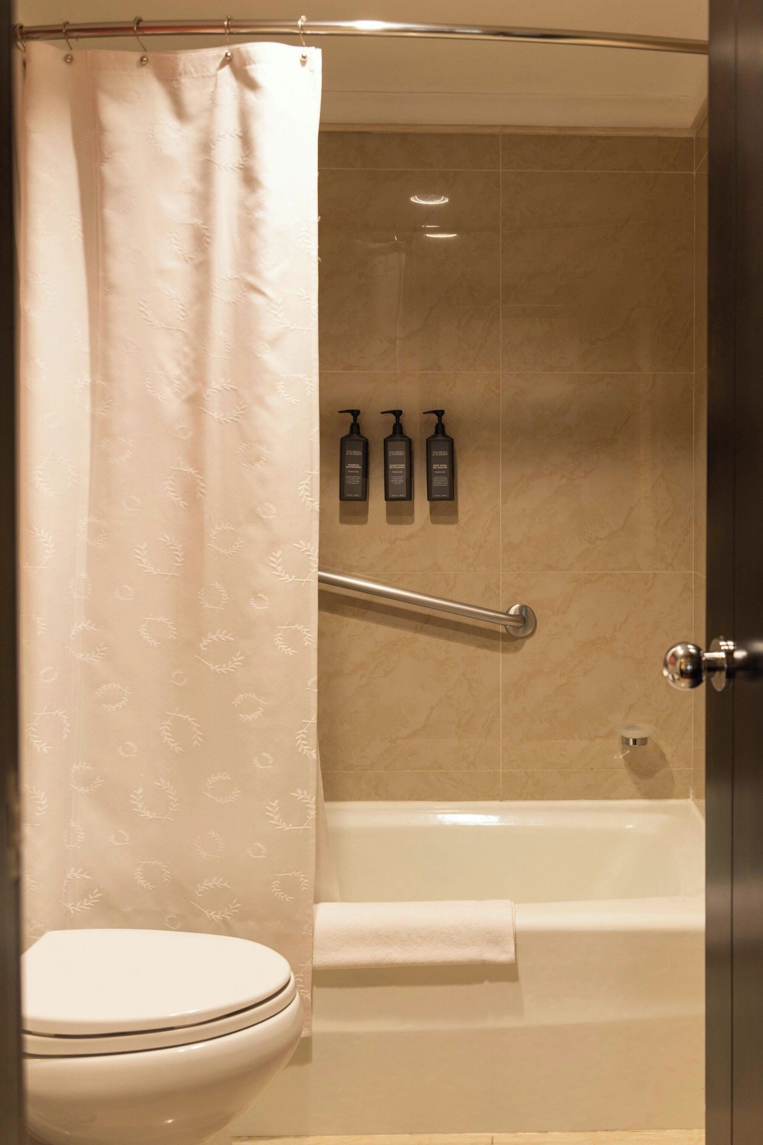 A bathroom with a toilet, a shower with a glass door, and three bottles of shampoo on the wall.