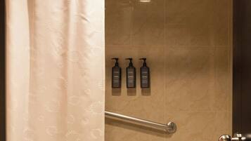 A bathroom with a toilet, a shower with a glass door, and three bottles of shampoo on the wall.