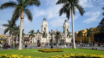 A historic plaza with a prominent church featuring two bell towers, surrounded by palm trees and a well-maintained flower bed.