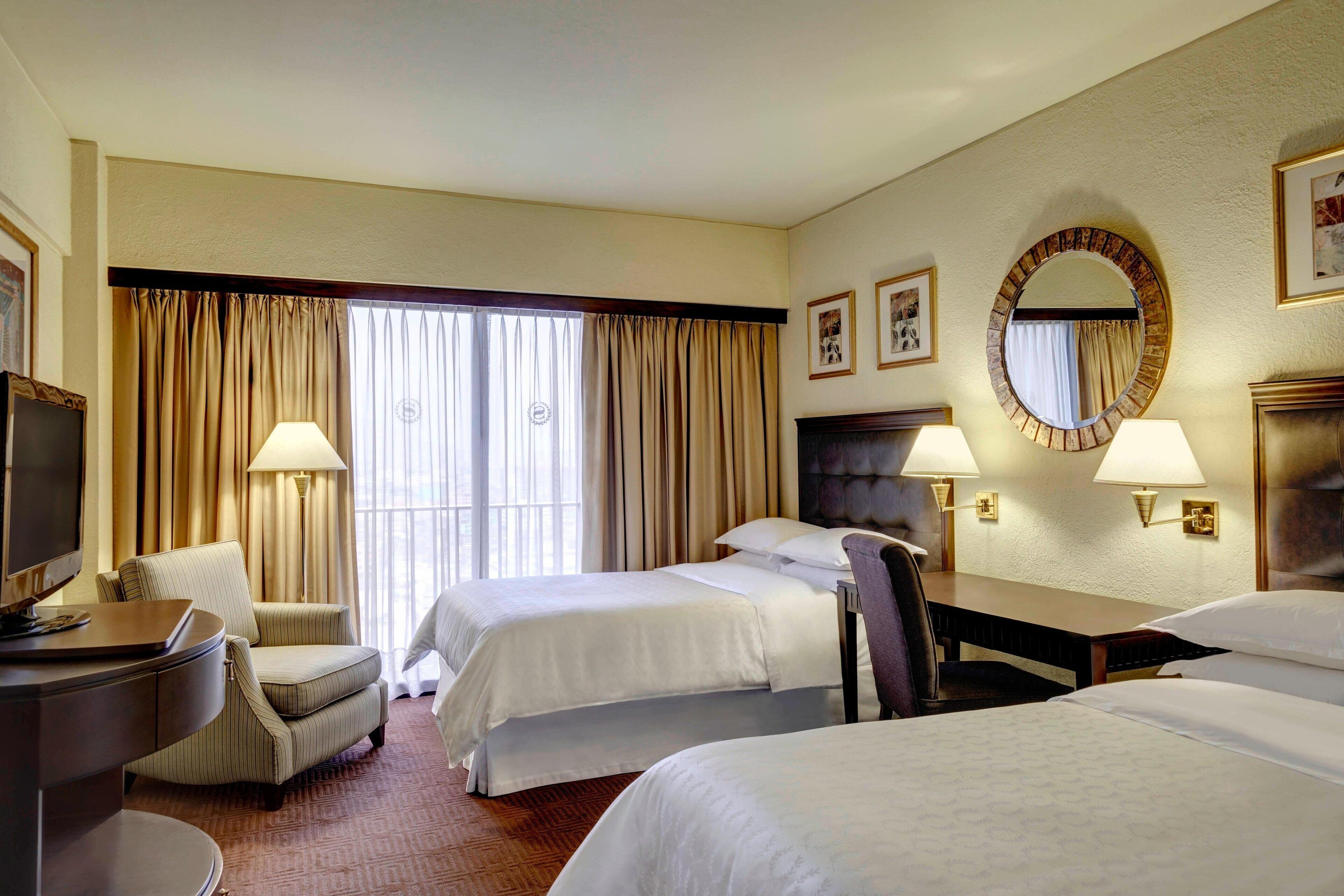 A hotel room with two beds, a desk, a chair, and a television.